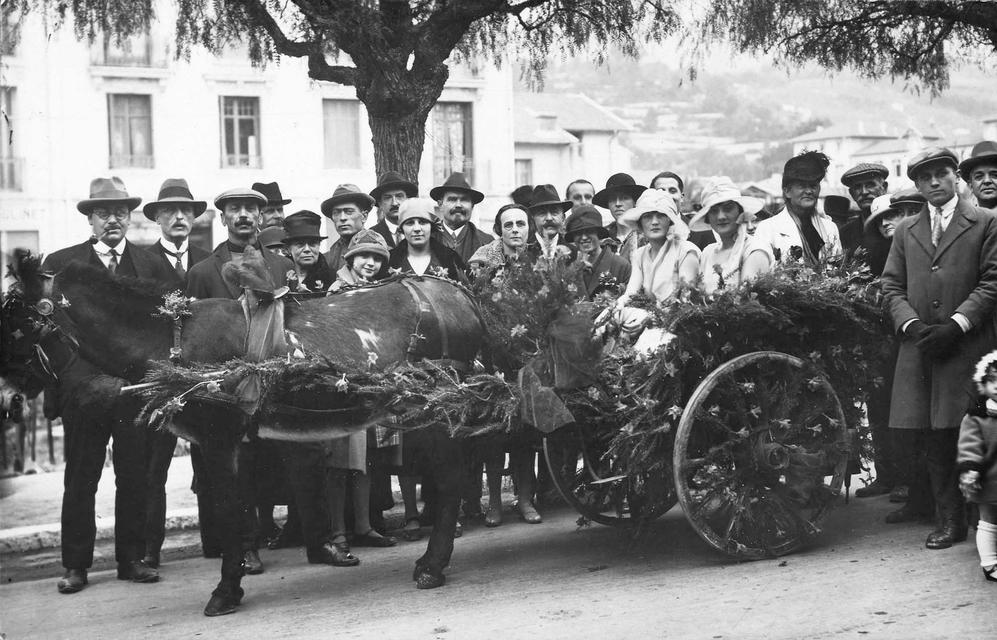 Til højre bag den blomstersmykkede æselkærre står Charlotte Trap de Thygeson, yderst til højre Carl Nielsen. Imellem dem stikker Margrete Rosenberg hatten frem. Sendt som postkort fra Menton, jf. 524.