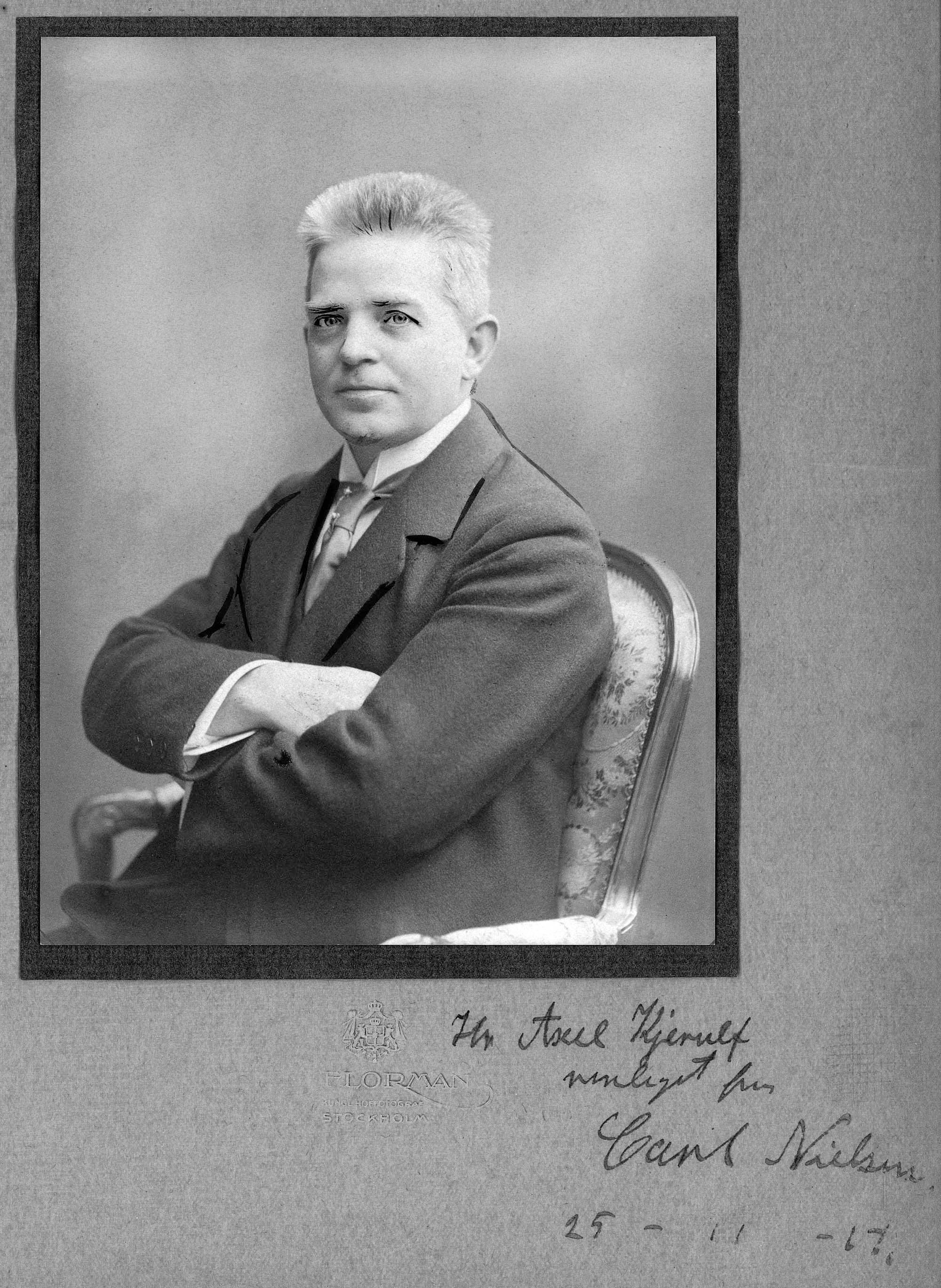 Carl Nielsen fotograferet i Stockholm oktober 1913 [Sml. 4:812], her med retoucheringer ved øjne og revers til avisbrug i anledning af koncerten den 29.11.1917 [Jf. 5:548]. To dage før bragte Politiken et interview med komponisten ved Charles Kjerulfs søn Axel Kjerulf (Samtid nr. 56); Af billedets dedikation kan man slutte at interviewet fandt sted den 25.11.1917.